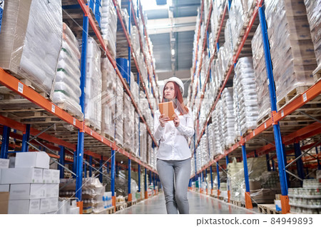 Woman with tablet looking attentively at shelves in warehouse Woman with tablet looking attentively at shelves in warehouse 84949893