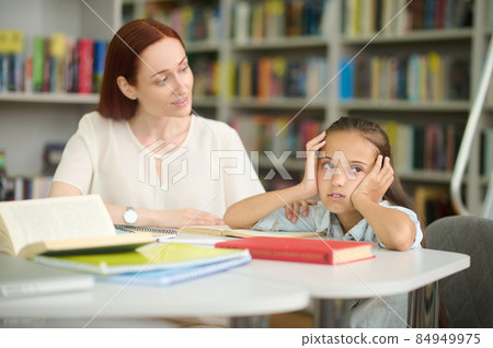 Woman looking questioningly at tired girl studying at table Woman looking questioningly at tired girl studying at table 84949975