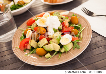 fresh salad of arugula, avocado, cherry tomatoes with olives and quail eggs on brown plate fresh salad of arugula, avocado, cherry tomatoes with olives and quail eggs on brown plate 84950083