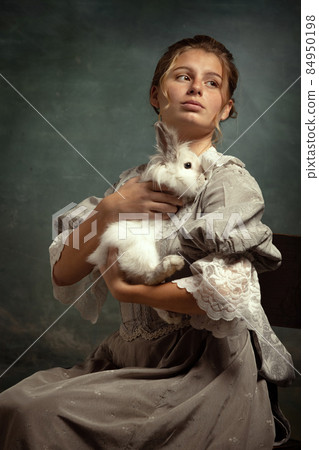 Portrait of young beautiful girl in gray dress of medieval style sitting with fluffy rabbit isolated on dark background. Portrait of young beautiful girl in gray dress of medieval style sitting with fluffy rabbit isolated on dark background. 84950198