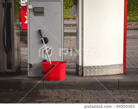 Red plastic bucket with mop at gas station Red plastic bucket with mop at gas station 84950303