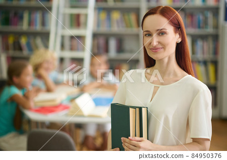 Woman holding books standing in library Woman holding books standing in library 84950376