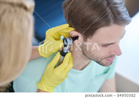 Female hands with otoscope near mans ear Female hands with otoscope near mans ear 84950382
