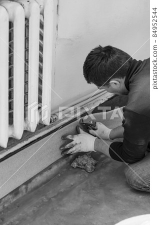 The man glues a damping tape on a wall bottom, protection for a floor coupler. 84952544