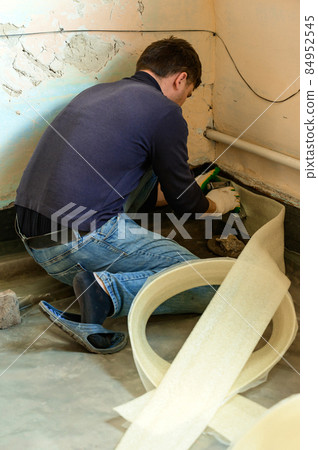 The man glues a damping tape on a wall bottom, protection for a floor coupler. 84952545
