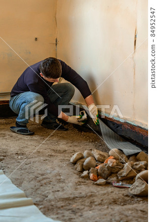 The worker attaches a bitumen tape with a stapler to protect the wood and floor from water. The worker attaches a bitumen tape with a stapler to protect the wood and floor from water. 84952547