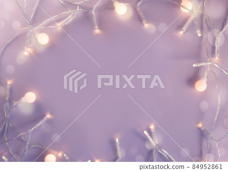 Festive backdrop for a postcard or web design. Frame made of a garland and bokeh lights on violet blue trendy background. New Year, Christmas or Birthday theme backplate. Color of the year 84952861