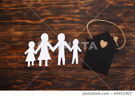 Happy paper cut family holding hands on wooden background near little toy house 84952907