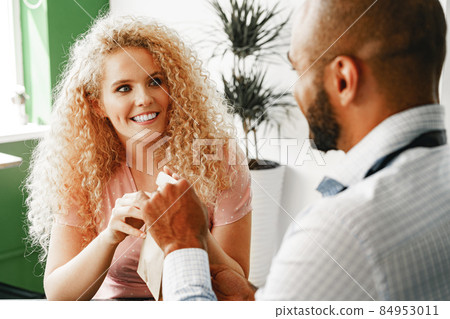 Smiling blonde woman talking to a waiter of a coffee shop at the counter Smiling blonde woman talking to a waiter of a coffee shop at the counter 84953011