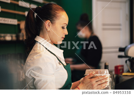 Young barista woman wearing apron holding tray with ready coffee Young barista woman wearing apron holding tray with ready coffee 84953338