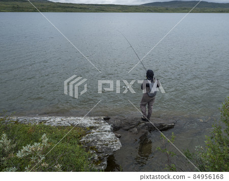 Man fisherman angler on lake shore fly fishing and caught trout or char fish in Gieddavrre lake in Sweden Lapland on Padjelantaleden hiking trail. 84956168