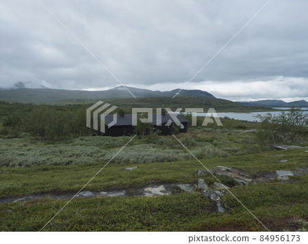 Lapland landscape at Virihaure lake with sami village Staloluokta houses and cottage, snow capped mountains and birch trees. Sweden summer moody and foggy wild nature, Padjelantaleden hiking trail. 84956173