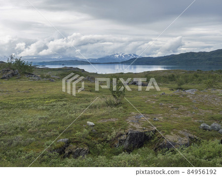 Lapland landscape at Virihaure lake with winding river, green mountains, birch trees and plain with big boulders. Sweden summer moody and foggy wild nature, Padjelantaleden hiking trail. 84956192