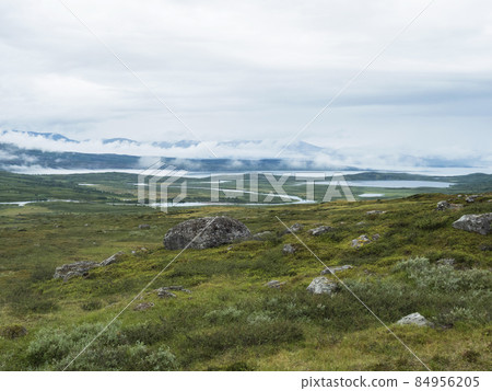Lapland landscape at Virihaure lake with winding river, green mountains, birch trees and plain with big boulders. Sweden summer moody and foggy wild nature, Padjelantaleden hiking trail. 84956205