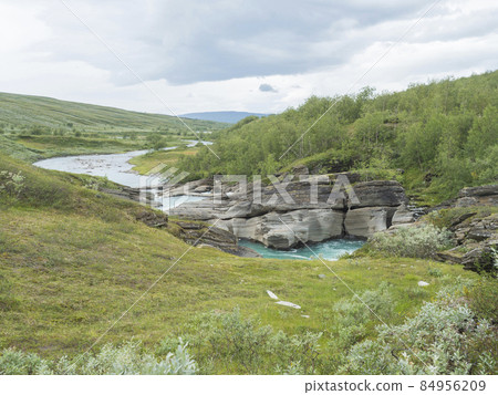 Valley with winding Laddejahka river, birch tree forest and green mountains. Lapland landscape Sweden at Padjelantaleden hiking trail. Summer moody sky 84956209