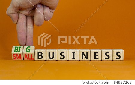 Big or small business symbol. Businessman turns wooden cubes, changes words small business to big business. Beautiful orange background, copy space. Big or small business concept. 84957265
