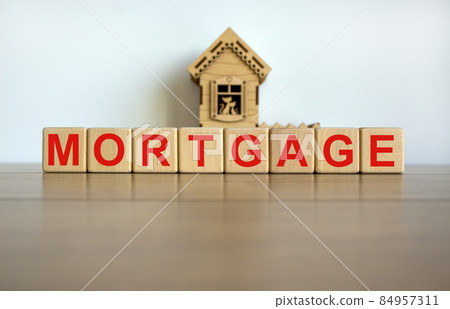 Wooden cubes form the word 'mortgage' near miniature house. Wooden table. Beautiful white background, copy space. Wooden cubes form the word 'mortgage' near miniature house. Wooden table. Beautiful white background, copy space. 84957311