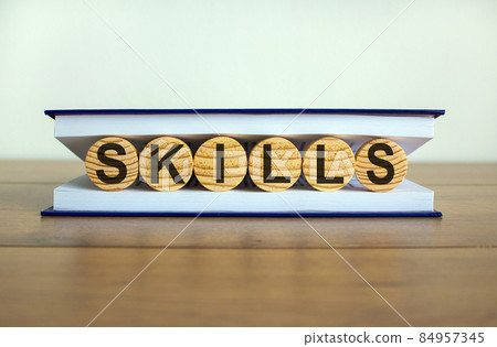 Concept word 'skills' on wooden circles between pages of a book on a beautiful wooden table. White background. Business concept. Concept word 'skills' on wooden circles between pages of a book on a beautiful wooden table. White background. Business concept. 84957345