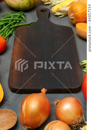 Wooden cutting board and scattered vegetables on dark background 84957554