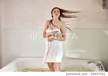 Woman dressed in towel stands in whirlpool bath. Woman dressed in towel stands in whirlpool bath. 84957581
