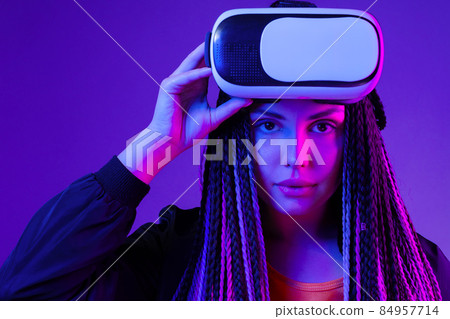 Young woman with afro braids using VR glasses on dark purple neon background 84957714