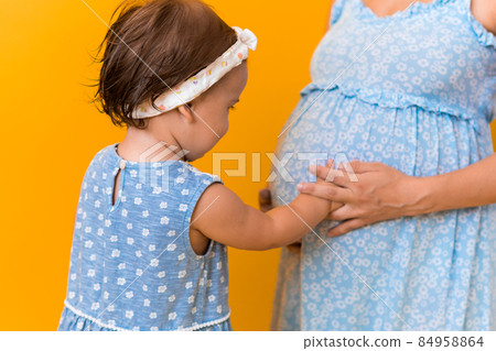 Motherhood, love, Childhood, hot summer - croped portrait pregnant mother unrecognizable woman blue dress little sibling girl sister hug touch mum big belly brother on yellow background copy space Motherhood, love, Childhood, hot summer - croped portrait pregnant mother unrecognizable woman blue dress little sibling girl sister hug touch mum big belly brother on yellow background copy space 84958864