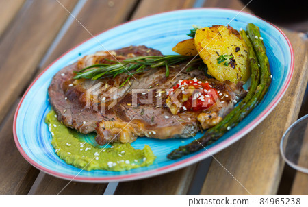Grilled veal loin with guacamole and vegetables on wooden background Grilled veal loin with guacamole and vegetables on wooden background 84965238