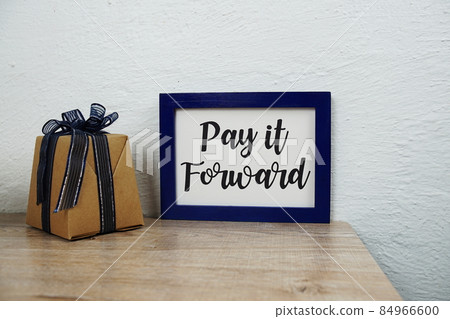 Pay it forward text and gift box on wooden table and white wall background 84966600