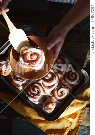A man lays out homemade cinnabons buns on a plate of baking dish. Top view. A man lays out homemade cinnabons buns on a plate of baking dish. Top view. 84967294