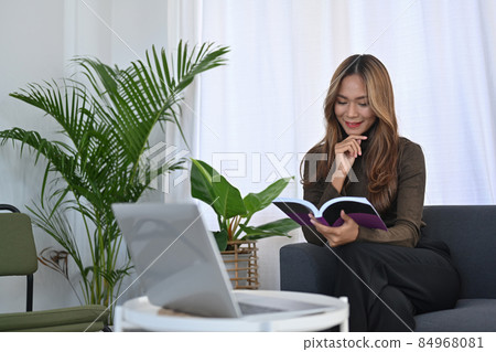 Charming asian woman sitting on sofa and reading book. 84968081