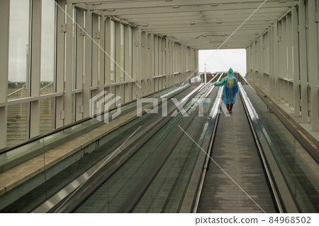 A woman in a raincoat rises on an escalator. Girl in protective clothing from the rain. Back view. 84968502