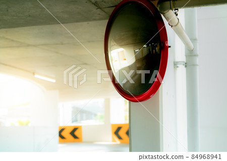 Convex safety mirror at curve of indoor car parking lot to reduce risk of accidents from blind corner or blind spots. Convex circular safety mirror in multi-level parking garage. Indoor traffic convex 84968941