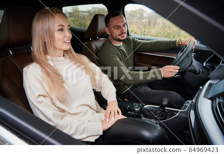 Happy man and woman traveling in car. Beautiful young couple sitting on front passenger seats and smiling while handsome man driving comfortable automobile. Happy man and woman traveling in car. Beautiful young couple sitting on front passenger seats and smiling while handsome man driving comfortable automobile. 84969423
