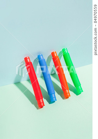 The straight folded pop tube stands leaning against the wall. Modern still life with antistress toy 84970559