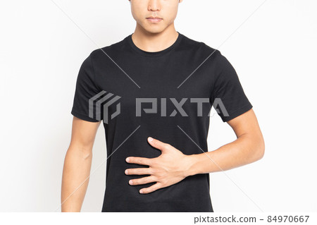 A man wearing a black T-shirt standing in front of a white background and putting his hands on his stomach A man wearing a black T-shirt standing in front of a white background and putting his hands on his stomach 84970667