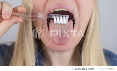 Clean tongue. Close-up of a woman performing antimicrobial hygiene with a special tongue brush. Isolated on white background. A blond female looks into the frame, as if he is looking in a mirror. Clean tongue. Close-up of a woman performing antimicrobial hygiene with a special tongue brush. Isolated on white background. A blond female looks into the frame, as if he is looking in a mirror. 84972002