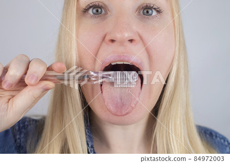 Clean tongue. Close-up of a woman performing antimicrobial hygiene with a special tongue brush. Isolated on white background. A blond female looks into the frame, as if he is looking in a mirror. Clean tongue. Close-up of a woman performing antimicrobial hygiene with a special tongue brush. Isolated on white background. A blond female looks into the frame, as if he is looking in a mirror. 84972003