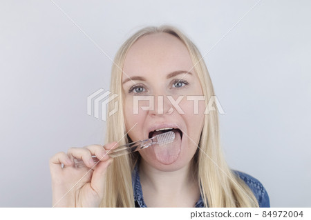 Clean tongue. Close-up of a woman performing antimicrobial hygiene with a special tongue brush. Isolated on white background. A blond female looks into the frame, as if he is looking in a mirror. Clean tongue. Close-up of a woman performing antimicrobial hygiene with a special tongue brush. Isolated on white background. A blond female looks into the frame, as if he is looking in a mirror. 84972004