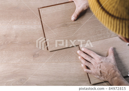 Installing laminate flooring in a room or office. Wooden parquet boards in the hands of a worker. Construction and decorative works for the finishing of housing Installing laminate flooring in a room or office. Wooden parquet boards in the hands of a worker. Construction and decorative works for the finishing of housing 84972815