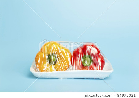 Vegetables in plastic packaging from the supermarket are minimal. Pepper in cellophane and non-degradable plastic on a blue background. Biodegradable product packaging, environmental protection 84973021