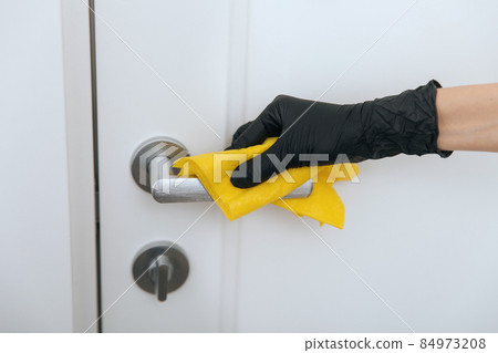 Cleaning door handle in black gloves with yellow wipe. Woman hand using towel for cleaning. Disinfection in hospital and public spaces against corona virus. Cleaning door handle in black gloves with yellow wipe. Woman hand using towel for cleaning. Disinfection in hospital and public spaces against corona virus. 84973208