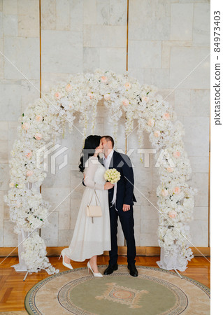 bride and groom in registry office kiss in an arch of flowers. bride and groom in registry office kiss in an arch of flowers. 84973403