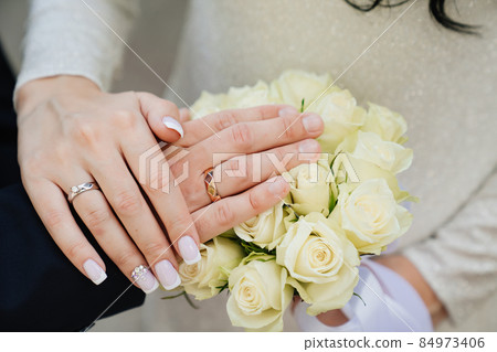 hands of man and woman with wedding rings on background of wedding bouquet. 84973406