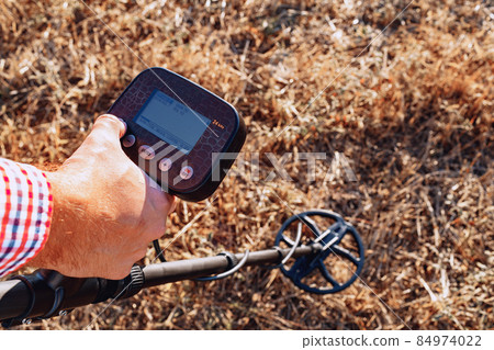 Male hand holding metal detector device above the ground Male hand holding metal detector device above the ground 84974022