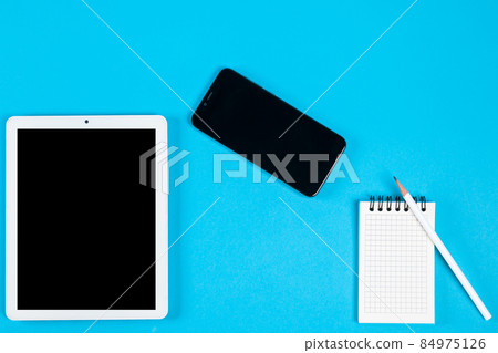 top view of workspace on a blue background. a notebook, pencil, smartphone and tablet computer with black screen top view of workspace on a blue background. a notebook, pencil, smartphone and tablet computer with black screen 84975126