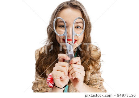 Close-up portrait of smiling young girl, dressmaker posing with scissors isolated on white background. Concept of job, hobby Close-up portrait of smiling young girl, dressmaker posing with scissors isolated on white background. Concept of job, hobby 84975156