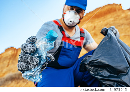 Hand of a man volunteer grabbing plastic litter into a waste bag cleaning up the beach Hand of a man volunteer grabbing plastic litter into a waste bag cleaning up the beach 84975945