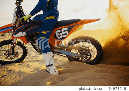 Motocross rider skidding wheel raising sand dust 84975946