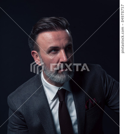 Portrait of a stylish elegant senior businessman with a beard and casual business clothes in photo studio isolated on dark background gesturing with hands Portrait of a stylish elegant senior businessman with a beard and casual business clothes in photo studio isolated on dark background gesturing with hands 84978757