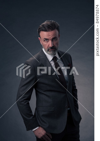Portrait of a stylish elegant senior businessman with a beard and casual business clothes in photo studio isolated on dark background gesturing with hands Portrait of a stylish elegant senior businessman with a beard and casual business clothes in photo studio isolated on dark background gesturing with hands 84978874